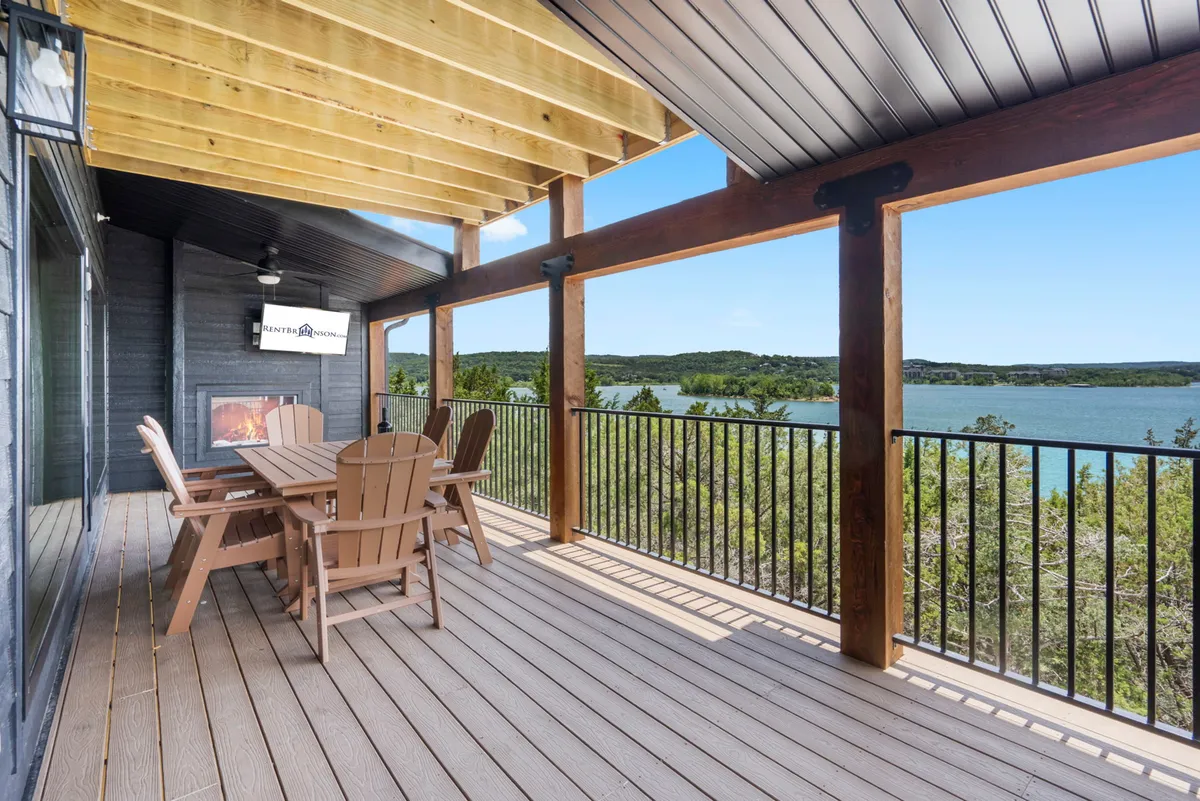 An outdoor dining table sits beneath sturdy wooden beams with a lantern-style light fixture, all set against a sweeping view of the lake. The atmosphere is tranquil, ideal for gatherings and soaking up the surrounding nature.