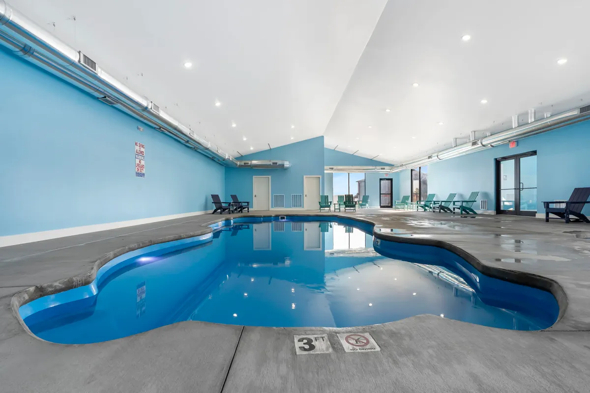 A serene indoor pool area with blue walls, lounge chairs, and bright lighting. The space feels rejuvenating, ideal for a relaxing swim regardless of the season.