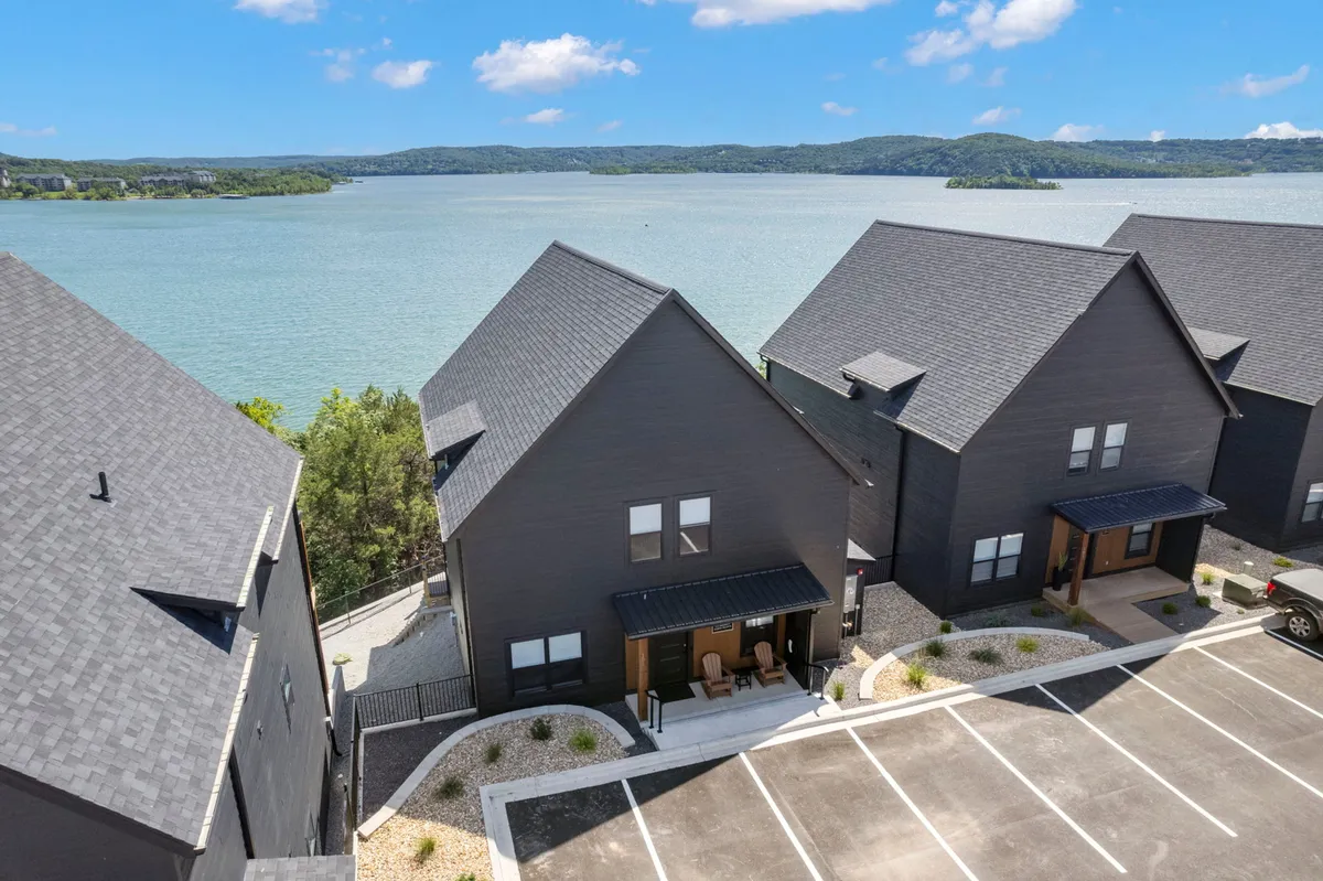 An exterior shot highlighting a modern home with large glass windows and a spacious outdoor seating area facing the lake. The foreground features comfortable chairs on the porch, while the background showcases peaceful water and trees.