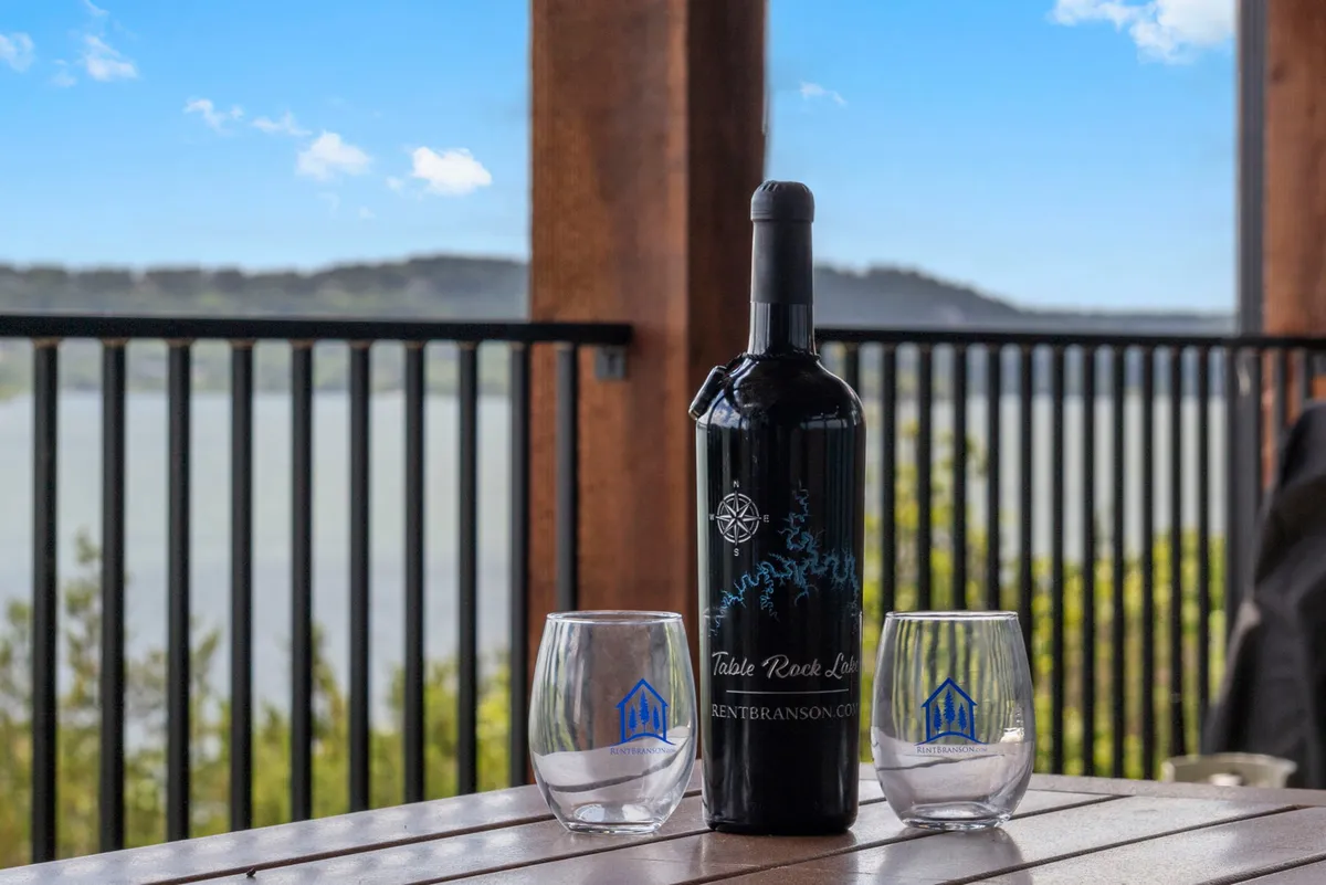 A scenic exterior setting with a bottle of wine and two glasses set on a table, framed by a breathtaking view overlooking the water at sunset. The intimate setup suggests opportunities for sunset gatherings, intimate conversations, or simply enjoying the peaceful lakeside environment.