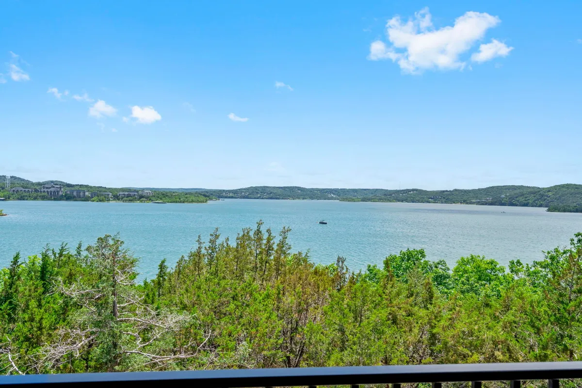 A serene lakeside view featuring calm water, lush greenery, and distant rolling hills under a clear blue sky. The landscape invites boating, fishing, hiking, and picnicking, and suggests ample outdoor space for both people and pets to explore and enjoy nature together.
