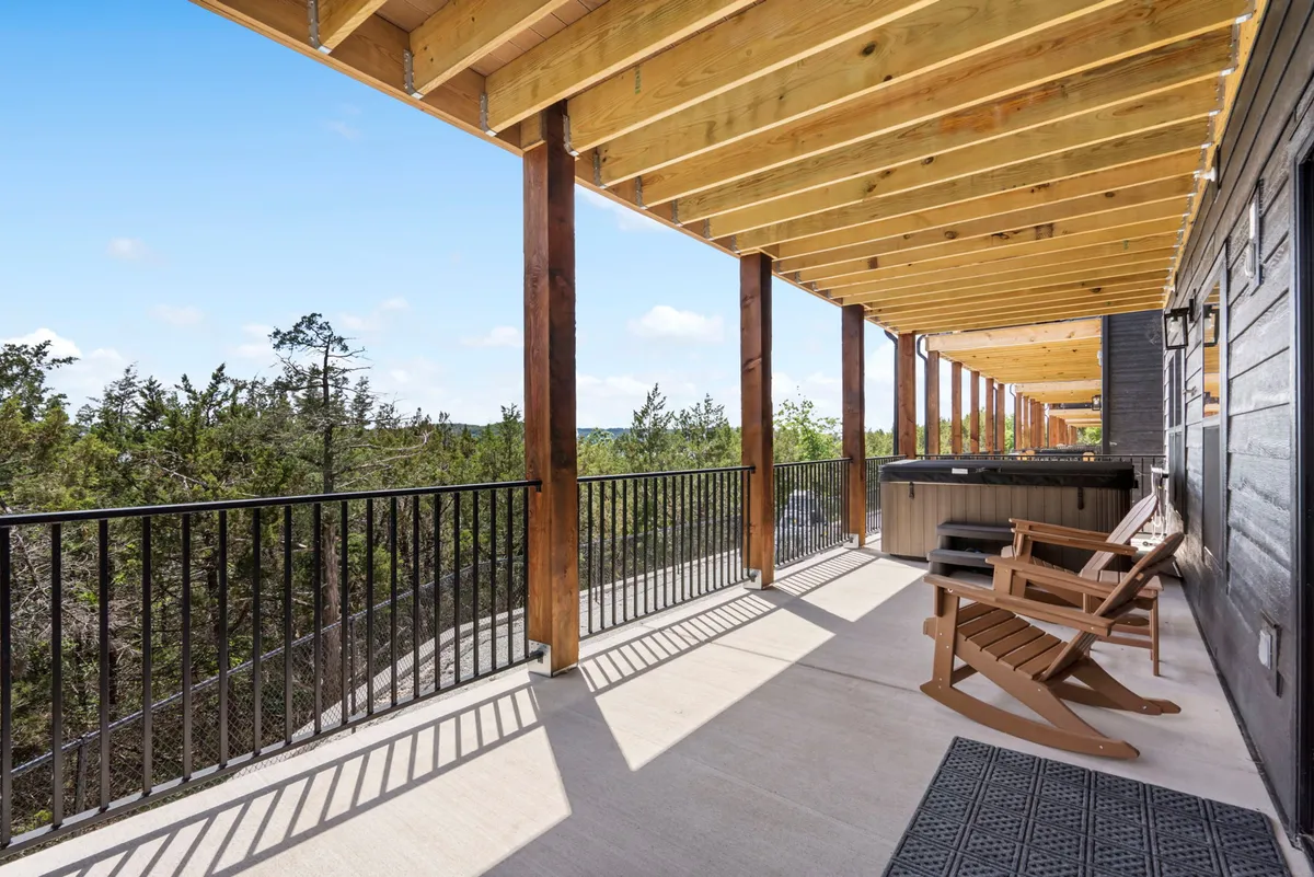 A tranquil wooden deck furnished with a hot tub and rocking chairs, bordered by railings and overlooking a scenic natural landscape. The space is designed for relaxation, socializing, and taking in the expansive views.