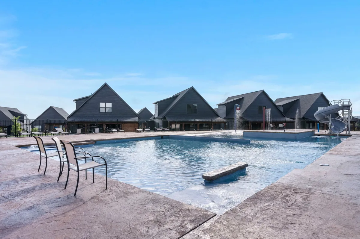 A vibrant exterior pool area featuring a swimming pool, water slide, surrounding buildings, and plenty of lounge chairs. The mood is cheerful, inviting families or groups to swim and enjoy the sun together.
