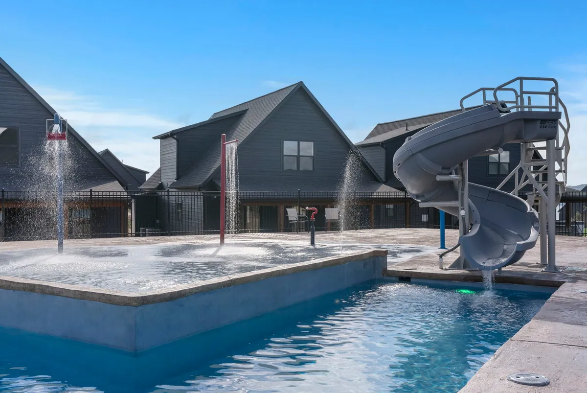 A lively exterior shot capturing the Rocky Shores resort pool area, featuring a swimming pool complete with a water slide and spray features. Families are seen enjoying the pool, and the surrounding cabins provide a sense of the community and upscale amenities at the resort.