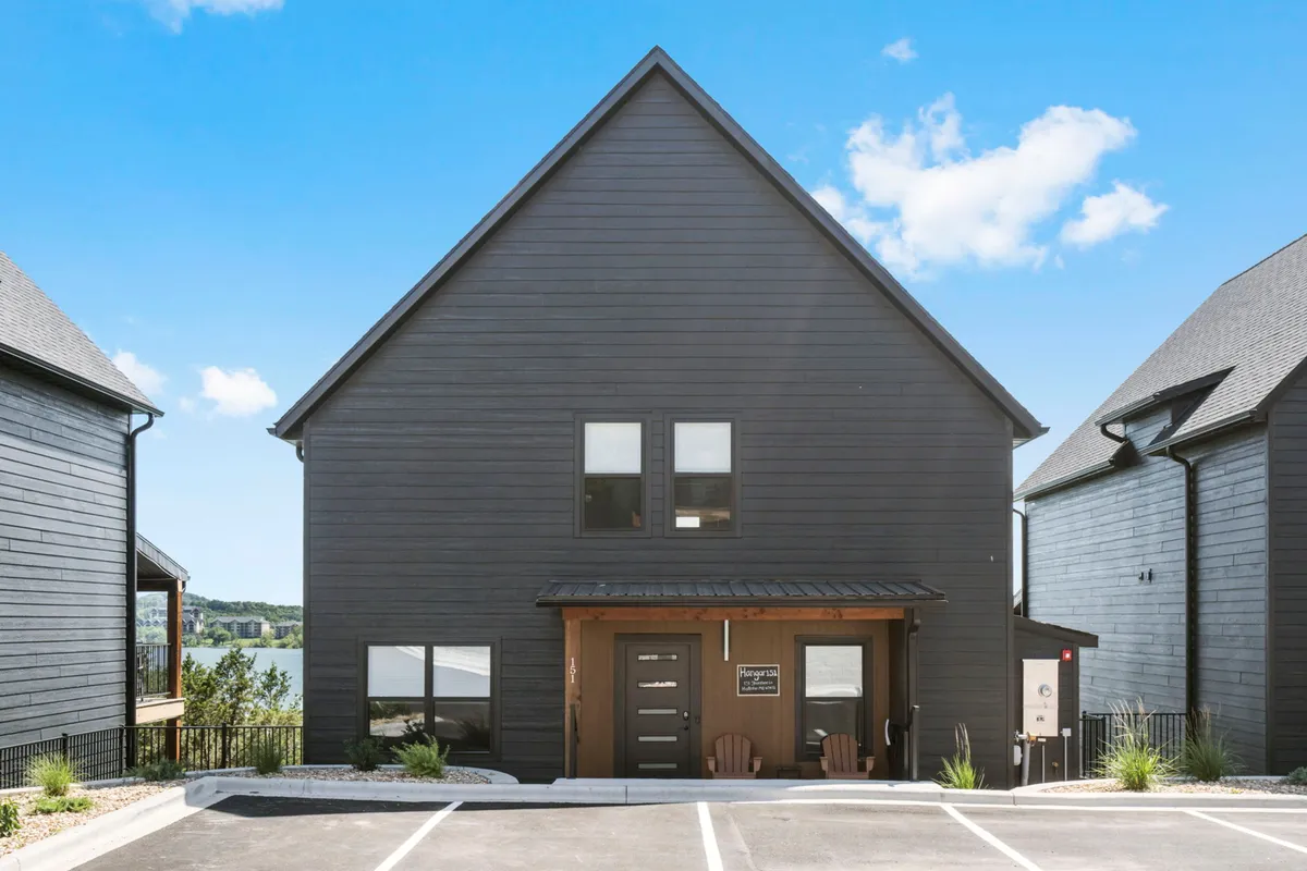 A serene exterior view of the property, with modern architecture, a wooden porch, and a lake view framed by landscaping—ideal for relaxing and socializing with family after a day of adventure.