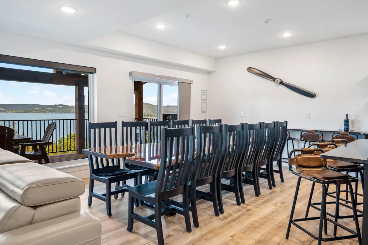 A large dining table sits beside a panoramic window with an impressive view, complemented by a decorative propeller on the wall and a nearby bar area with stools. The space feels communal and inviting, ideal for group meals and celebrations.